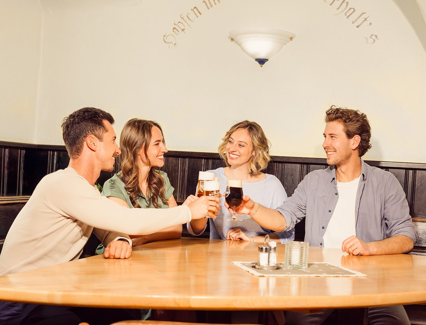 Eine Freundesgruppe sitzt im Hirter Braukeller Zwei Frauen und zwei Männer sitzen im Hirter Braukeller und stoßen mit Bier an.