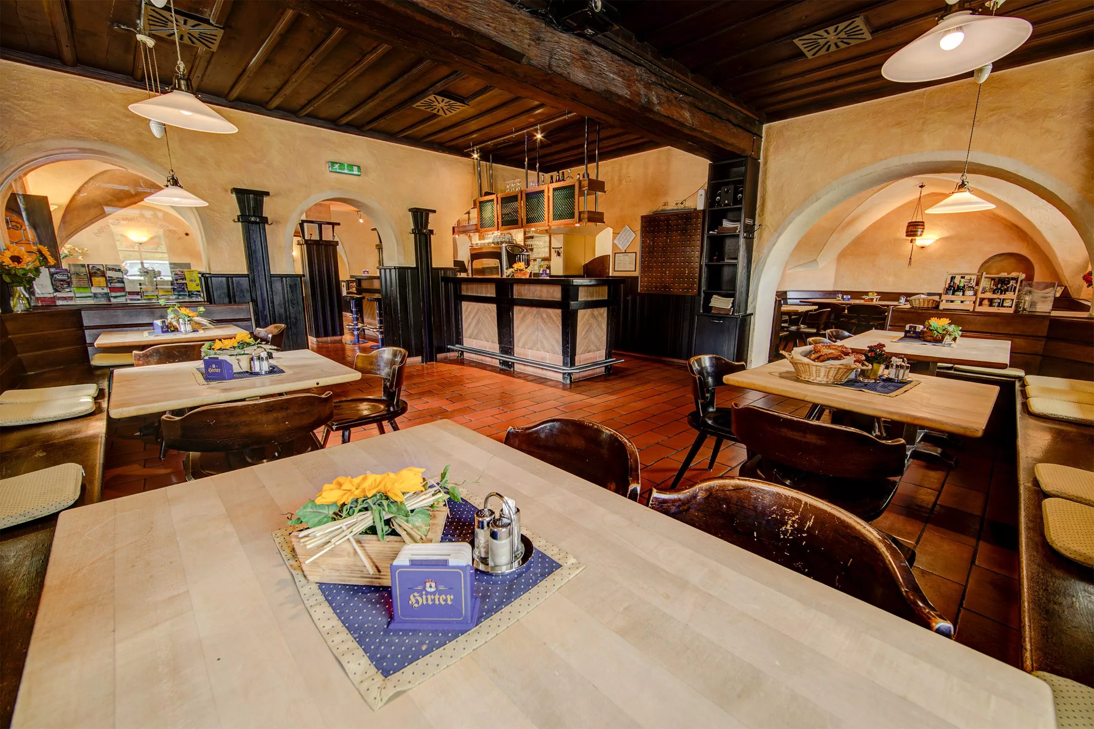 Ein Foto der Bierschwemme im Hirter Braukeller mit Tischen, einem Korb mit Brezen und der Theke im Hintergrund.